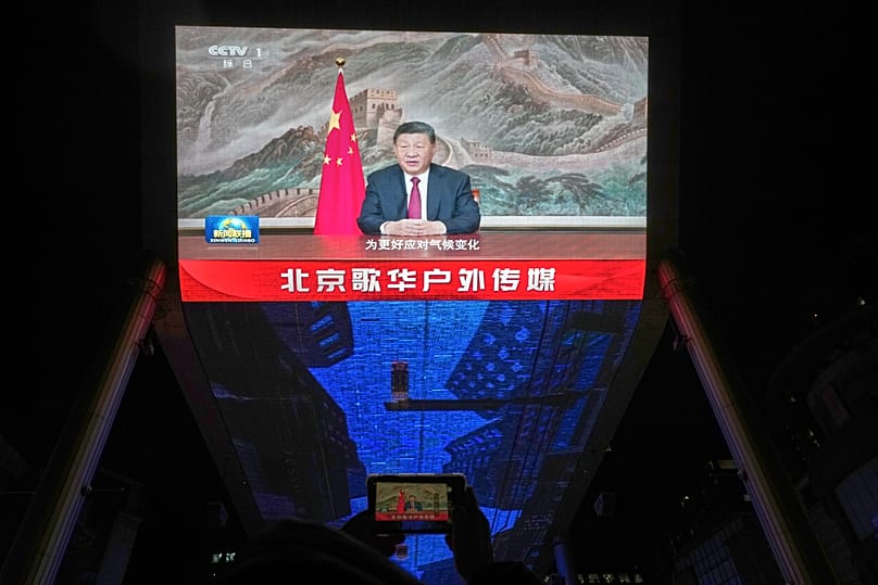 A resident uses her smartphone to film a large screen showing Chinese President Xi Jinping delivering his 2026 New Year message in Beijing, 31 December, 2025