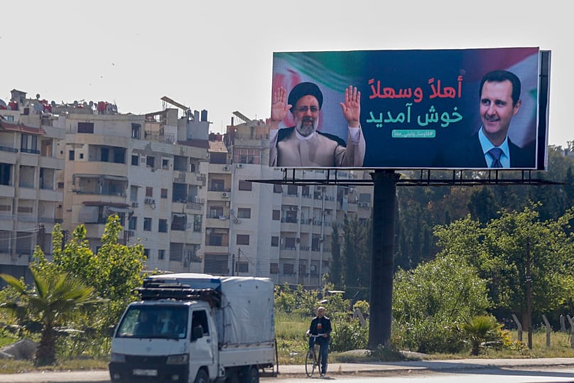 FILE: Cars pass under a poster with pictures of Iranian President Ebrahim Raisi and Syrian President Bashar al-Assad with Arabic that reads "Welcome," in Damascus, 3 May 2023