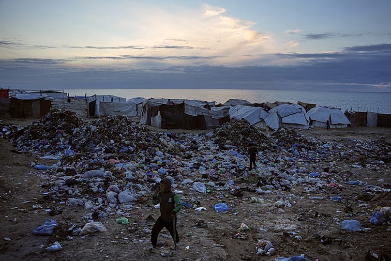 Children walk over a pile of garbage at a makeshift tent camp for displaced Palestinians on a beach in Deir al-Balah, in the Gaza Strip Friday, Jan. 16, 2026