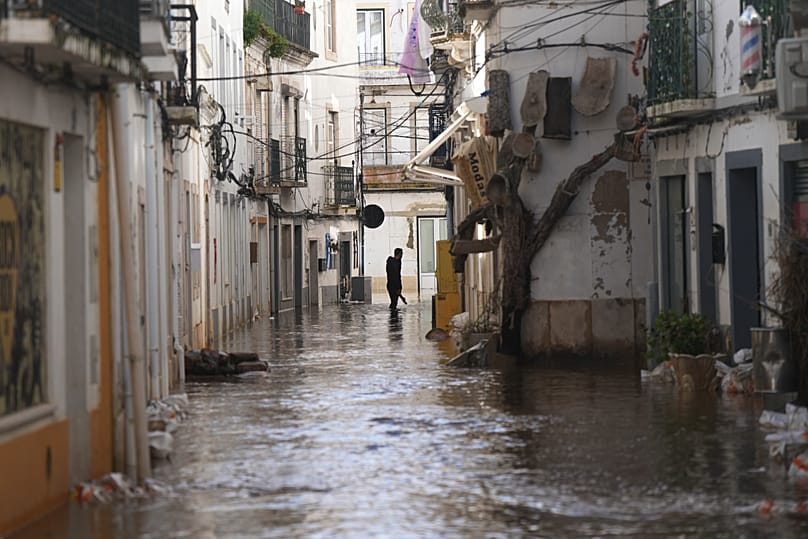 A residents walks along a flooded street after the Sado River overflowed following heavy rains in Alcácer do Sal, southern Portugal, Friday, Feb. 6, 2026.
