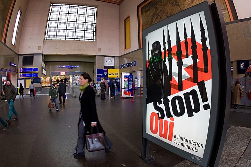 People walk by a poster from the right-wing Swiss People's Party depicting a woman wearing a burqa in front of a Swiss flag at the central station in Geneva, 4 November, 2009