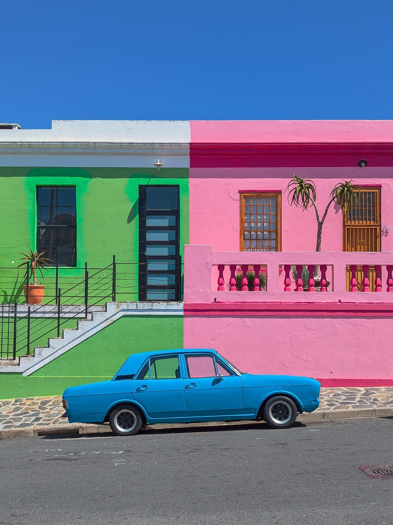 Colour Divides depicts the juxtaposition of a blue car against bright green and pink buildings of the Bo-Kaap neighbourhood in South Africa's Cape Town.