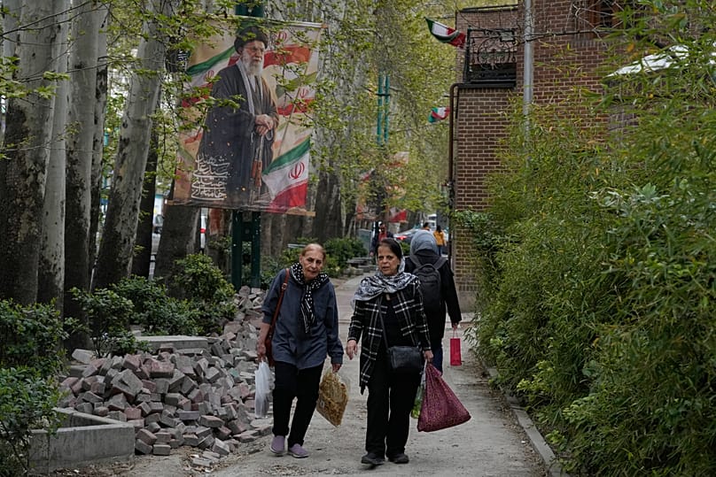 Women walk past a banner depicting the late Iranian Supreme Leader Ayatollah Ali Khamenei in northern Tehran, 12 April, 2026