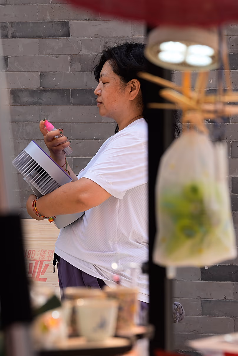 A shop assistant in her souvenir shop in Beijing sprays herself with water and cools down with a portable fan. Tuesday 2 June 2026.