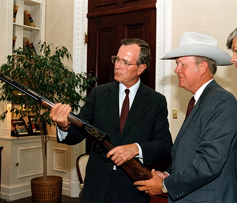 US Vice President George Bush holds a Winchester rifle gifted to him by Texas Sesquicentennial Wagon Train Association President Charles Oliver at the White House, 9 July 1986