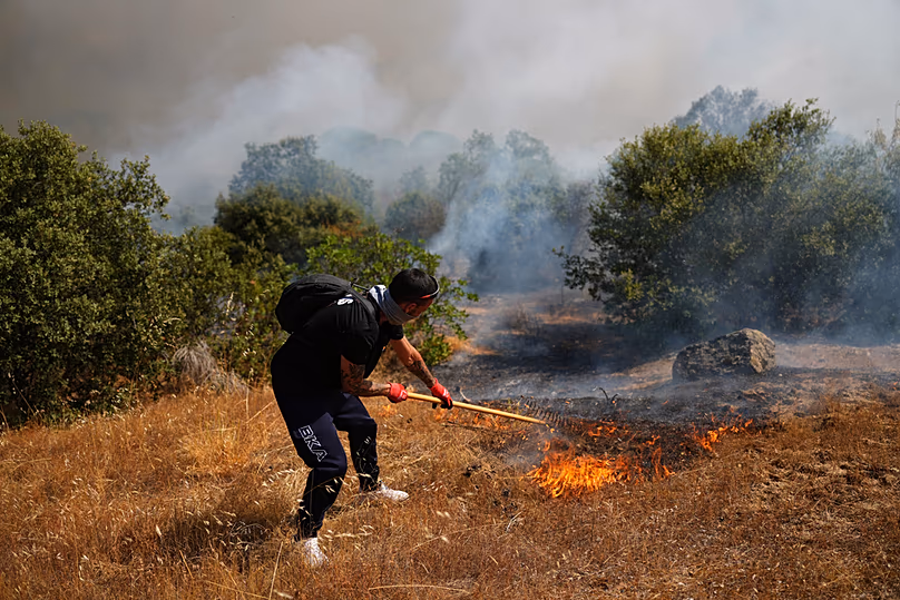 A volunteer uses a rake trying to help stop a wildfire from advancing in San Martin de Valdeiglesias, west of Madrid, Spain, Sunday, July 26, 2026