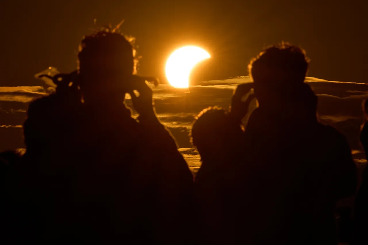 People watch a solar eclipse on the shore of the Gulf of Finland in St. Petersburg, Russia