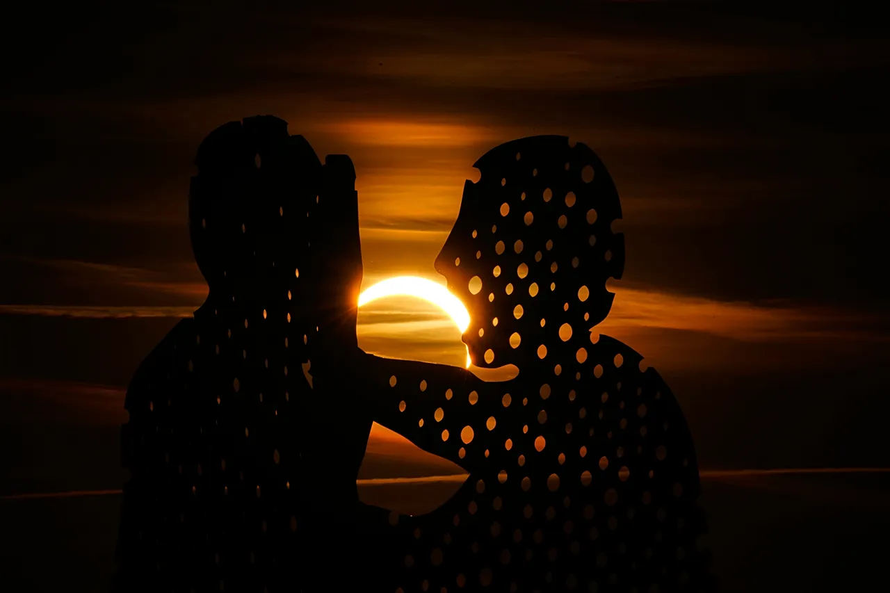 The moon partially covers the sun during solar eclipse near the Molecule Man sculpture in Berlin, Germany