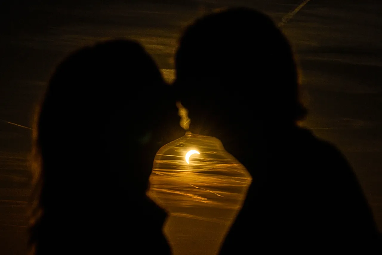 A couple kissees during a partial solar eclipse at the former airport Tempelhof in Berlin, Germany