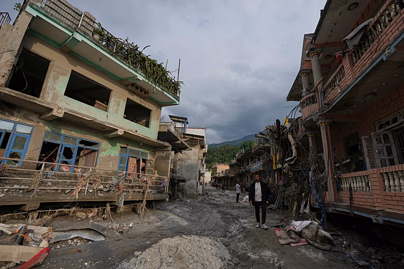 People walk along a street lined with damaged structures after flash flooding in the Devighat area of Nuwakot district in Nepal, 28 August, 2026