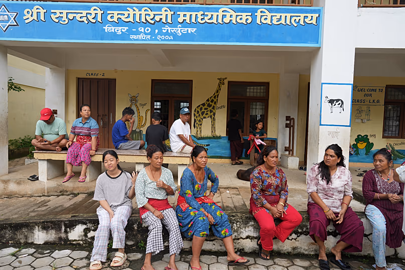 Flood survivors sit outside a school that has been turned into a temporary shelter following the floods in Bidur, 1 September, 2026