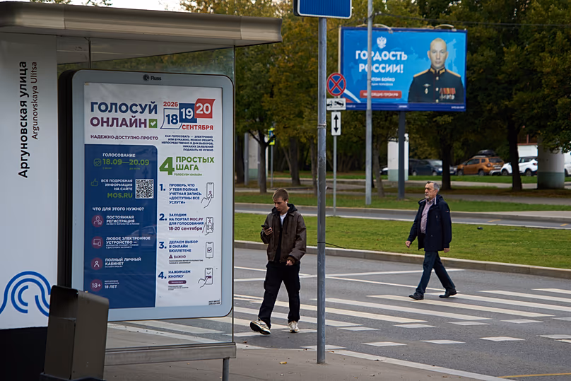 A poster advertising online voting in the elections; in the background a billboard shows a soldier with the slogan