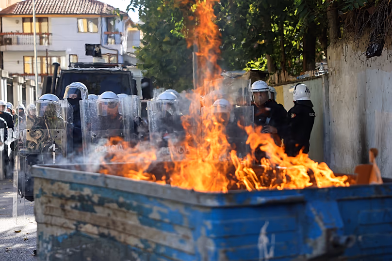 Riot police stand in formation behind a burning garbage can during an anti-government rally, in Tirana, Albania, Saturday, Oct. 24, 2026. (AP Photo/Hameraldi Agolli)